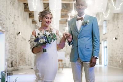 Allée décorée de fleurs blanches dans une salle en pierre éclairée par des guirlandes lumineuses.