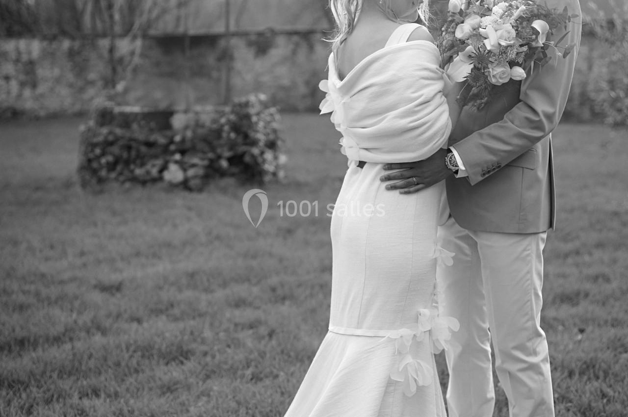Un couple en tenue de mariage se tient debout dans un jardin, échangeant un regard complice.