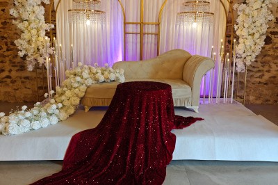 Allée décorée de fleurs blanches dans une salle en pierre éclairée par des guirlandes lumineuses.