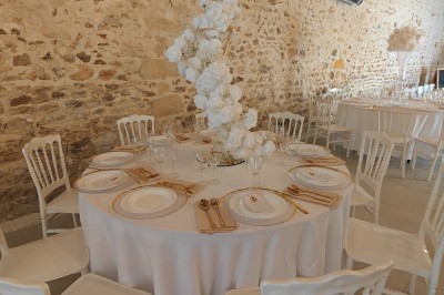 Allée décorée de fleurs blanches dans une salle en pierre éclairée par des guirlandes lumineuses.