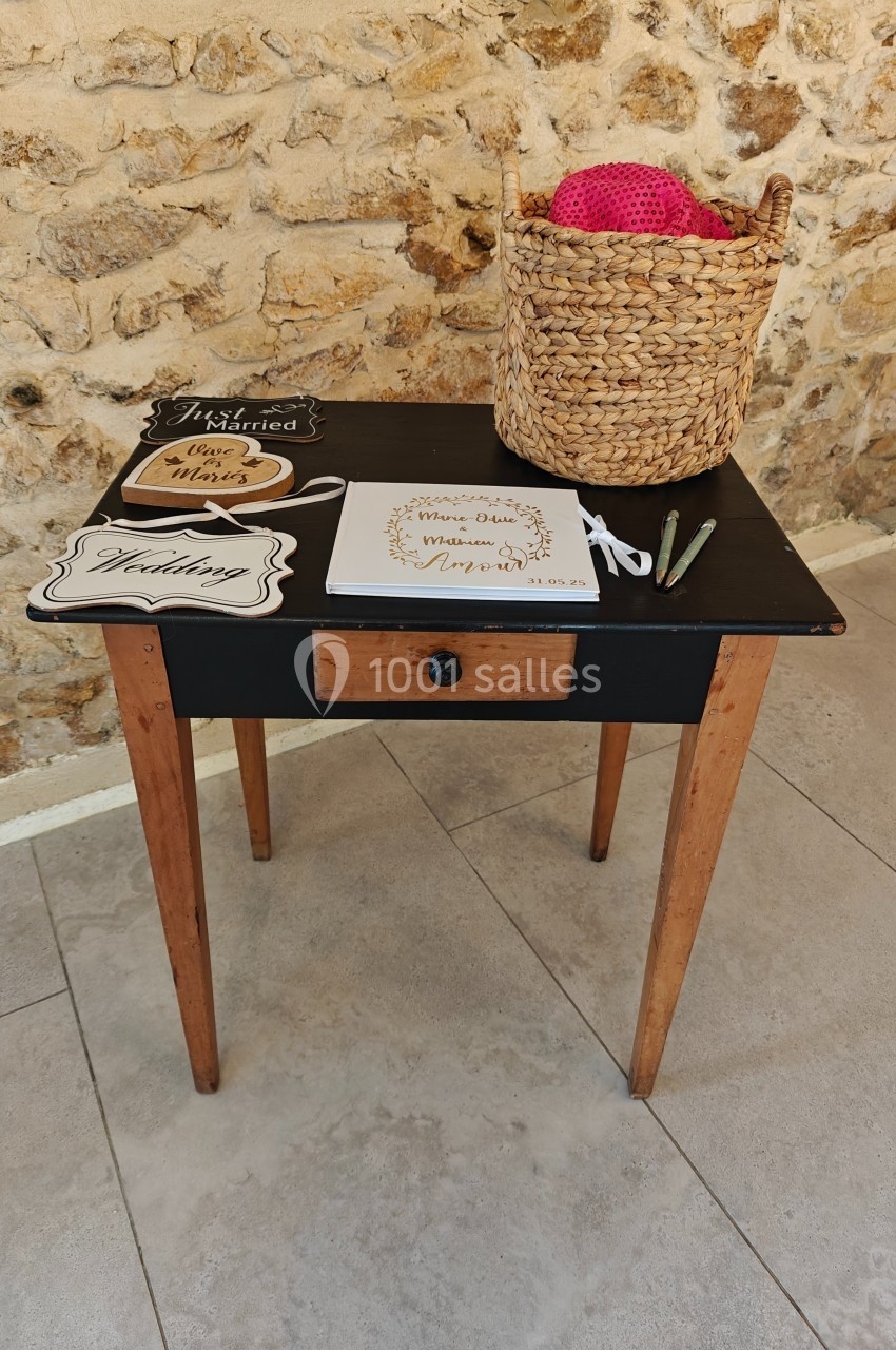Table en bois avec un tiroir, décorée de pancartes, d'un panier en osier contenant du fil rose et de stylos posés dessus.