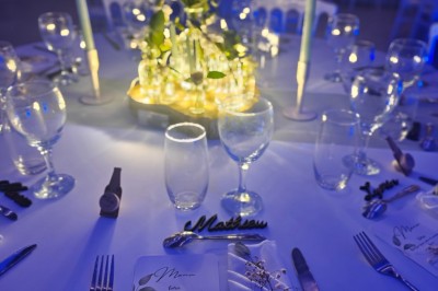 Allée décorée de fleurs blanches dans une salle en pierre éclairée par des guirlandes lumineuses.