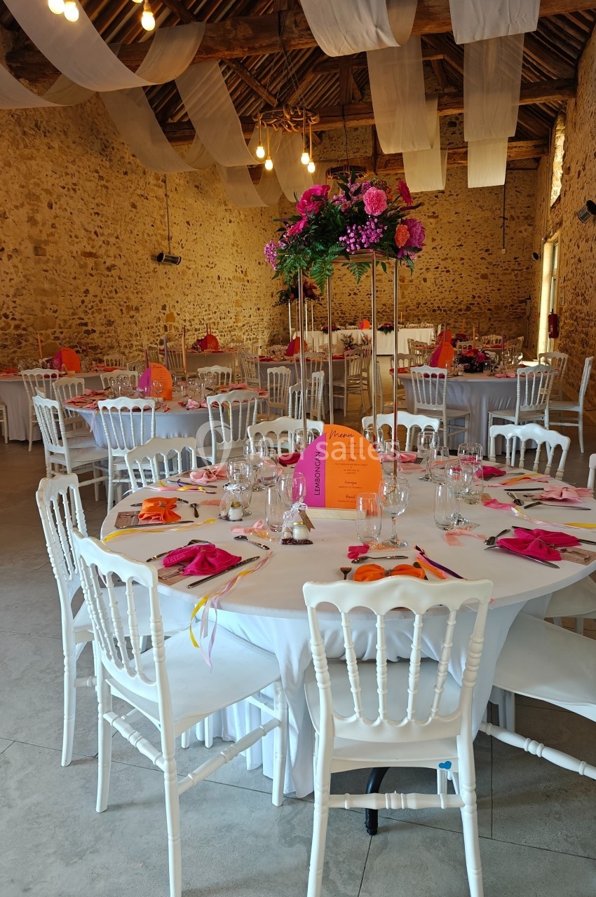 Salle de réception décorée avec des tables rondes, nappes blanches, chaises blanches et centres de table fleuris.