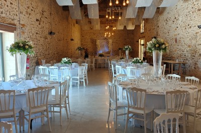 Allée décorée de fleurs blanches dans une salle en pierre éclairée par des guirlandes lumineuses.
