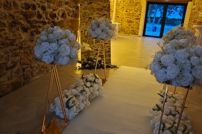 Allée décorée de fleurs blanches dans une salle en pierre éclairée par des guirlandes lumineuses.