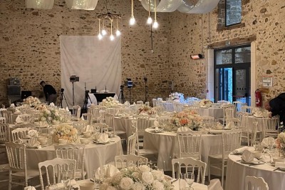 Allée décorée de fleurs blanches dans une salle en pierre éclairée par des guirlandes lumineuses.