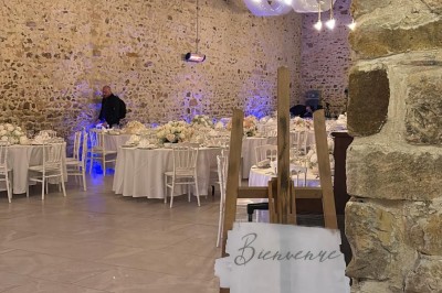 Allée décorée de fleurs blanches dans une salle en pierre éclairée par des guirlandes lumineuses.