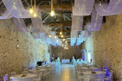 Allée décorée de fleurs blanches dans une salle en pierre éclairée par des guirlandes lumineuses.