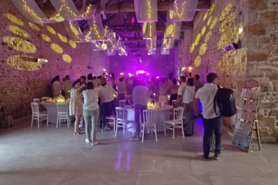 Allée décorée de fleurs blanches dans une salle en pierre éclairée par des guirlandes lumineuses.