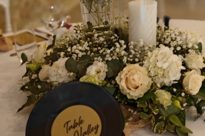 Allée décorée de fleurs blanches dans une salle en pierre éclairée par des guirlandes lumineuses.