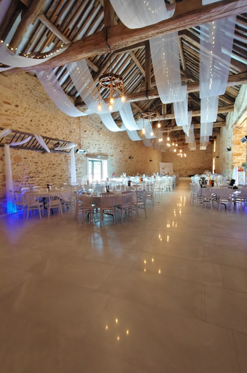 Salle de réception en pierre avec poutres apparentes, tables dressées et voilages suspendus au plafond.