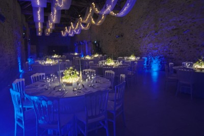 Allée décorée de fleurs blanches dans une salle en pierre éclairée par des guirlandes lumineuses.