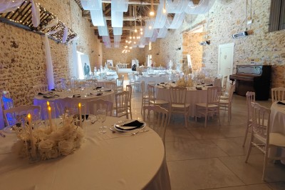 Allée décorée de fleurs blanches dans une salle en pierre éclairée par des guirlandes lumineuses.