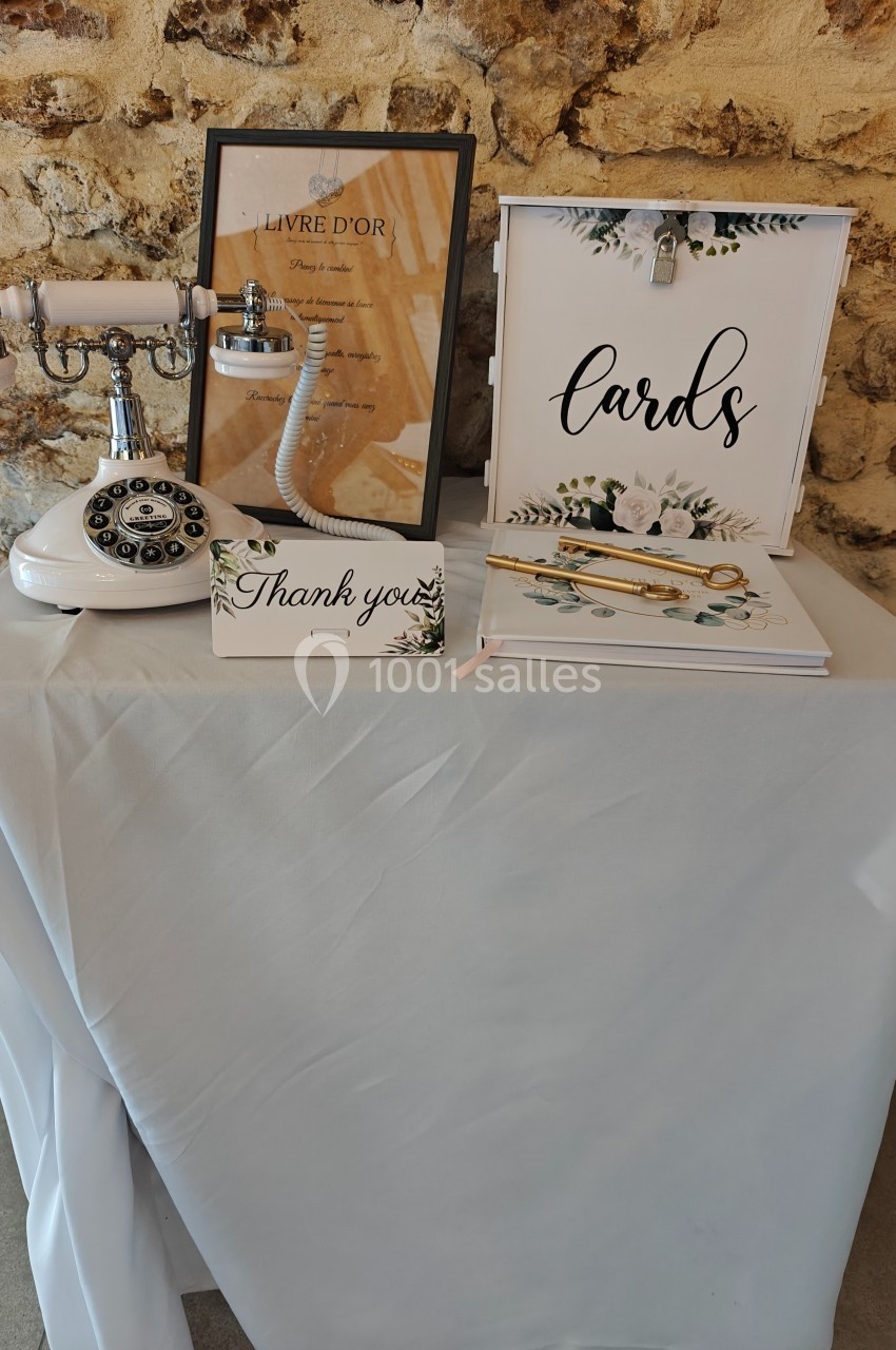 Table décorée avec un téléphone rétro, un livre d'or, une boîte à cartes et une carte ’Thank you’, devant un mur en pierre.