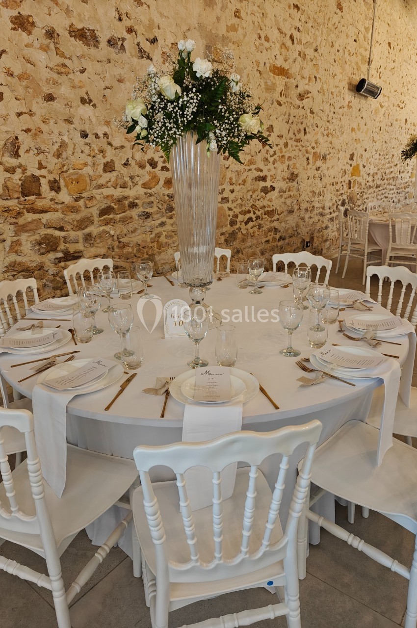 Table ronde décorée pour un événement, avec nappes blanches, vaisselle élégante et centre de table floral dans une salle en…