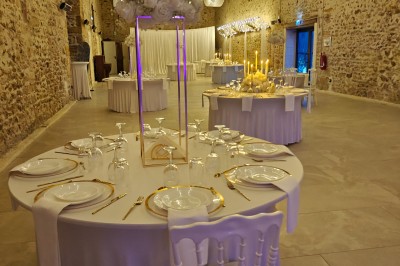 Allée décorée de fleurs blanches dans une salle en pierre éclairée par des guirlandes lumineuses.