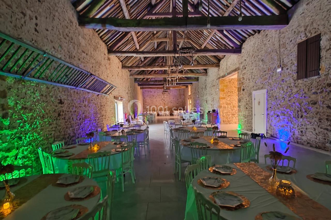 Salle de réception en pierre avec tables décorées, éclairage coloré et poutres apparentes au plafond.