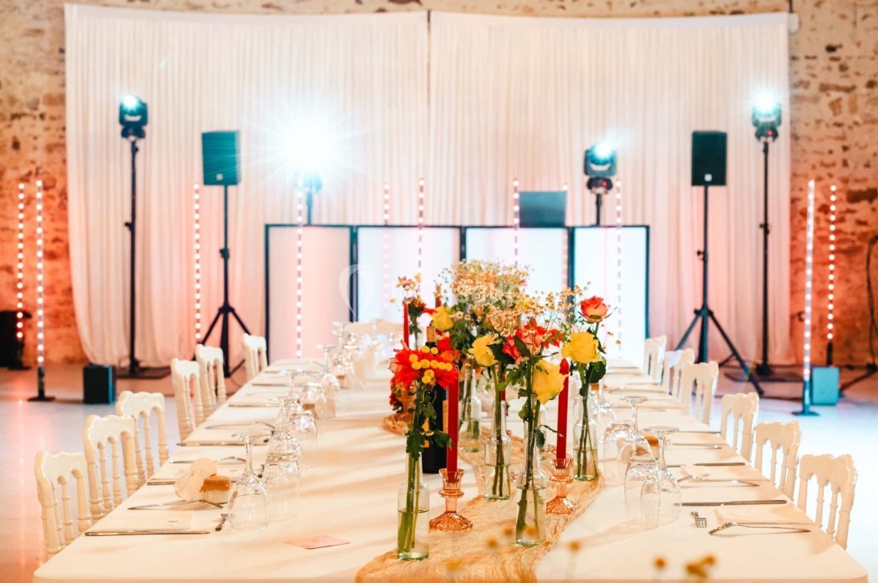 Grande table de réception décorée de fleurs colorées, avec un fond lumineux et des rideaux blancs.