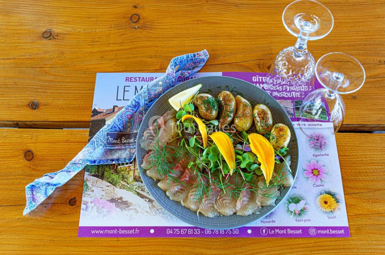 Assiette de carpaccio de poisson avec légumes, pommes de terre rôties et citron, servie sur une table en bois.