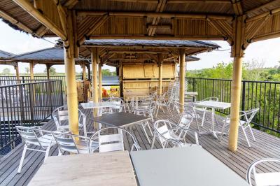 Grande terrasse couverte avec structure en bois, sol carrelé et quelques tables et chaises disposées près des ouvertures.