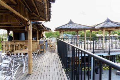 Grande terrasse couverte avec structure en bois, sol carrelé et quelques tables et chaises disposées près des ouvertures.