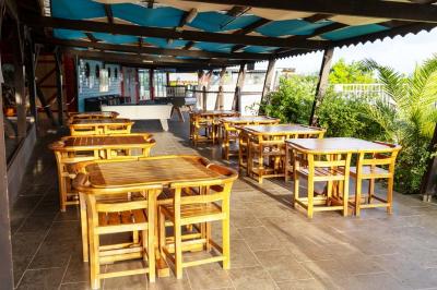 Grande terrasse couverte avec structure en bois, sol carrelé et quelques tables et chaises disposées près des ouvertures.