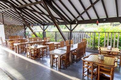 Grande terrasse couverte avec structure en bois, sol carrelé et quelques tables et chaises disposées près des ouvertures.