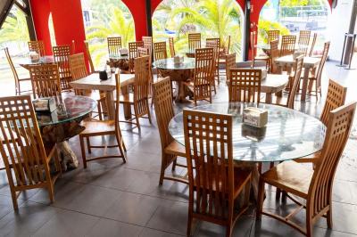 Grande terrasse couverte avec structure en bois, sol carrelé et quelques tables et chaises disposées près des ouvertures.