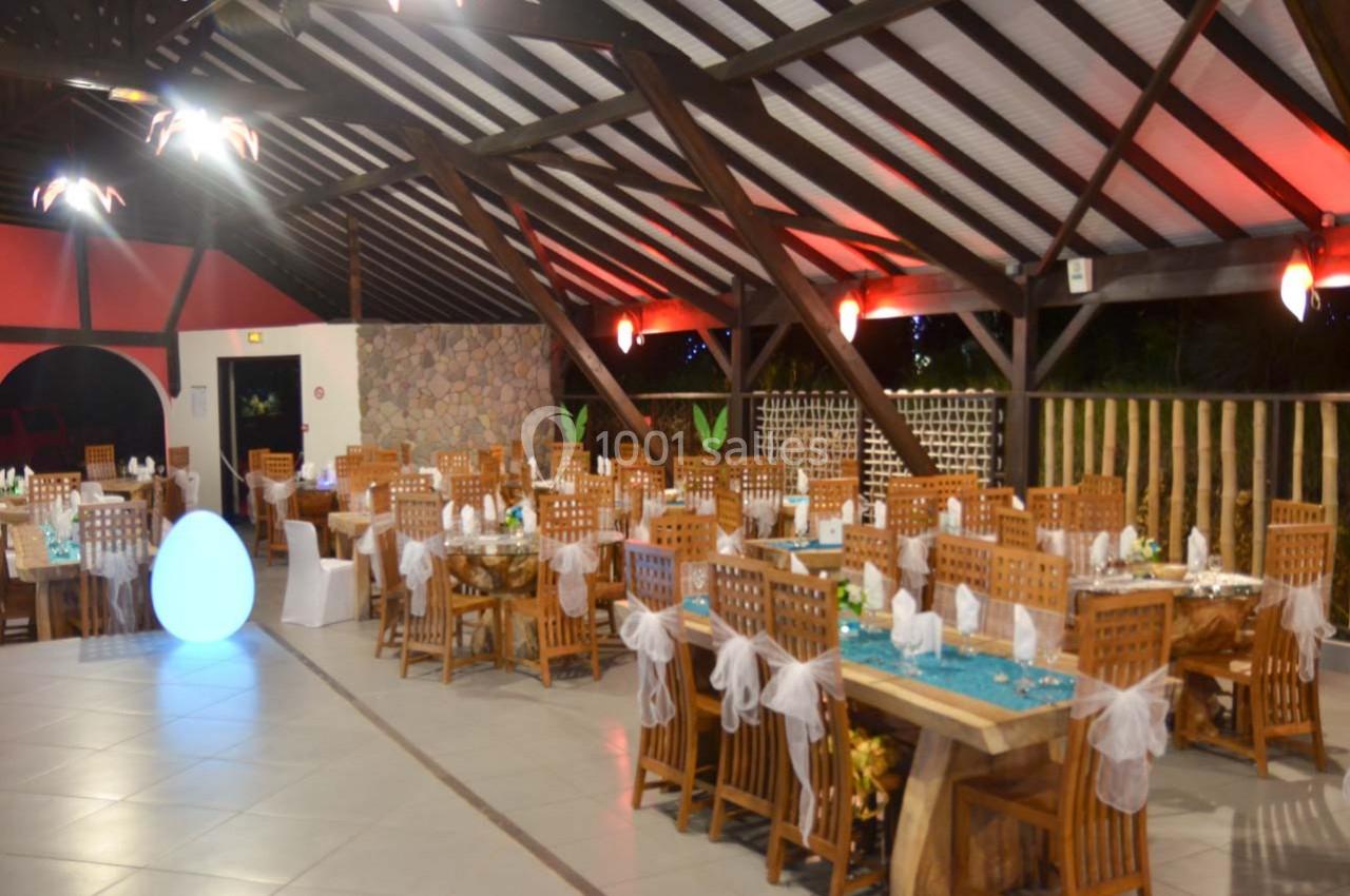 Salle de réception décorée avec des tables en bois, nappes turquoise et chaises ornées de nœuds blancs.
