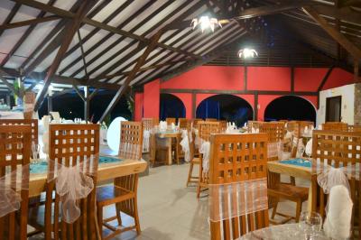 Grande terrasse couverte avec structure en bois, sol carrelé et quelques tables et chaises disposées près des ouvertures.