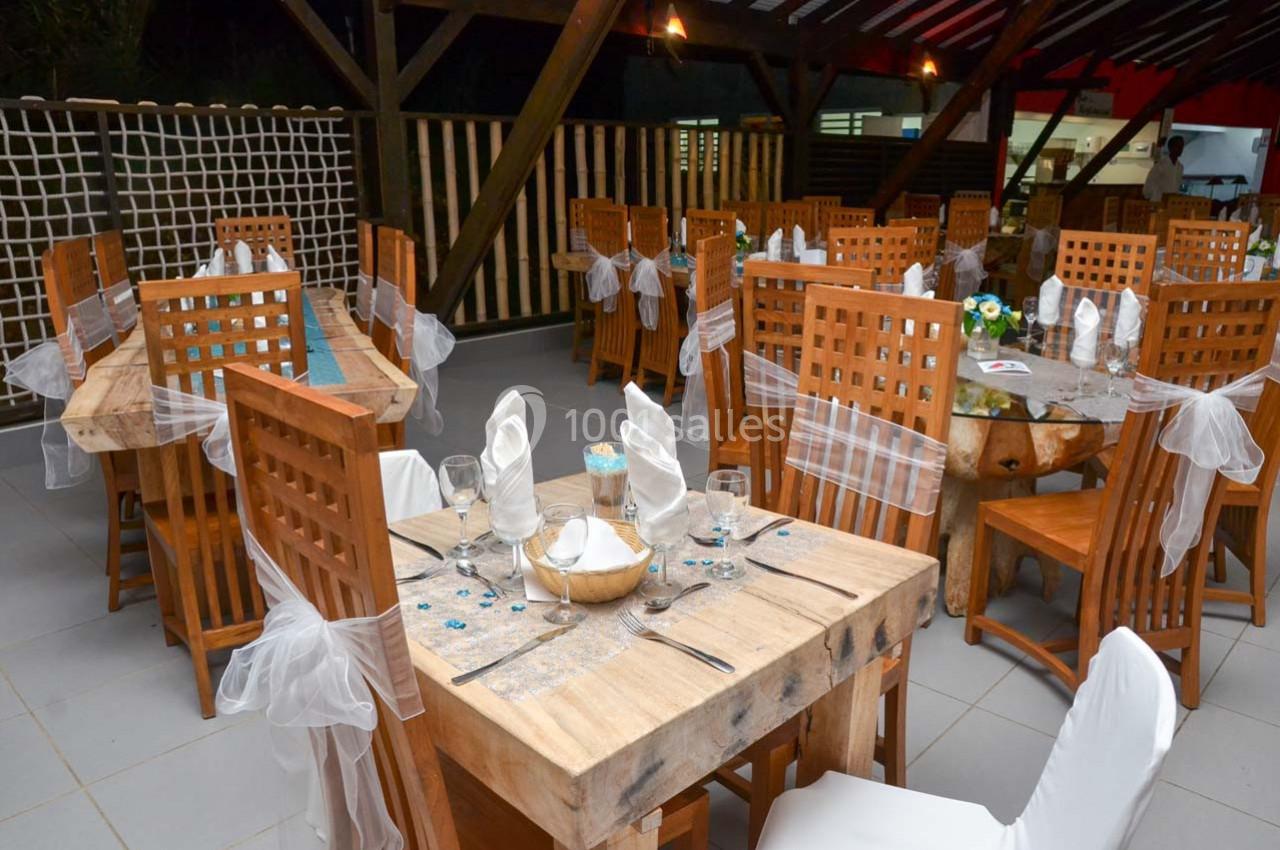 Salle de restaurant décorée avec des tables en bois, nappes blanches et chaises ornées de rubans translucides.
