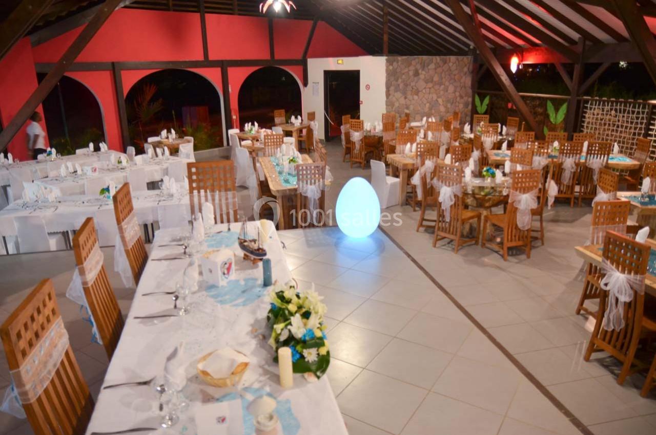 Salle de réception décorée avec des tables dressées, nappes blanches et chaises en bois, ambiance lumineuse et festive.