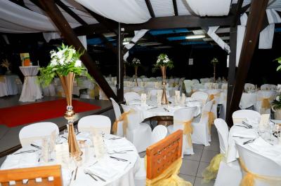 Grande terrasse couverte avec structure en bois, sol carrelé et quelques tables et chaises disposées près des ouvertures.