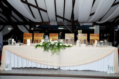 Grande terrasse couverte avec structure en bois, sol carrelé et quelques tables et chaises disposées près des ouvertures.