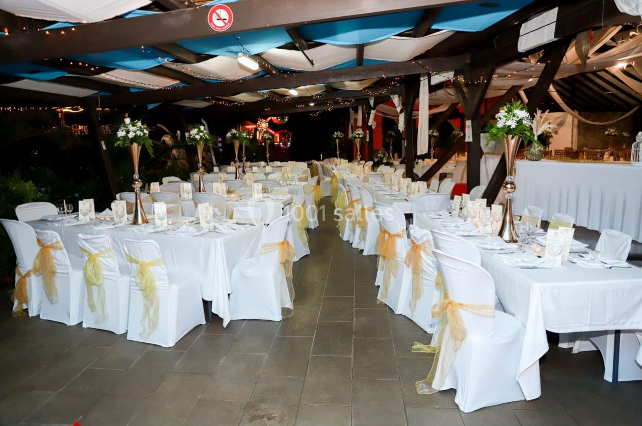 Salle de réception décorée avec des tables dressées, nappes blanches et chaises ornées de rubans jaunes.