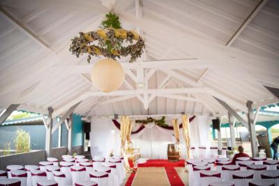 Grande terrasse couverte avec structure en bois, sol carrelé et quelques tables et chaises disposées près des ouvertures.