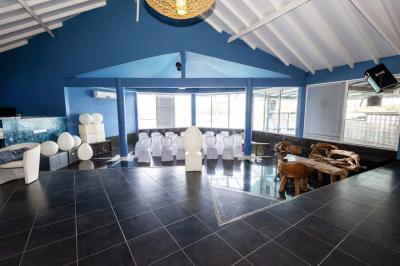 Grande terrasse couverte avec structure en bois, sol carrelé et quelques tables et chaises disposées près des ouvertures.