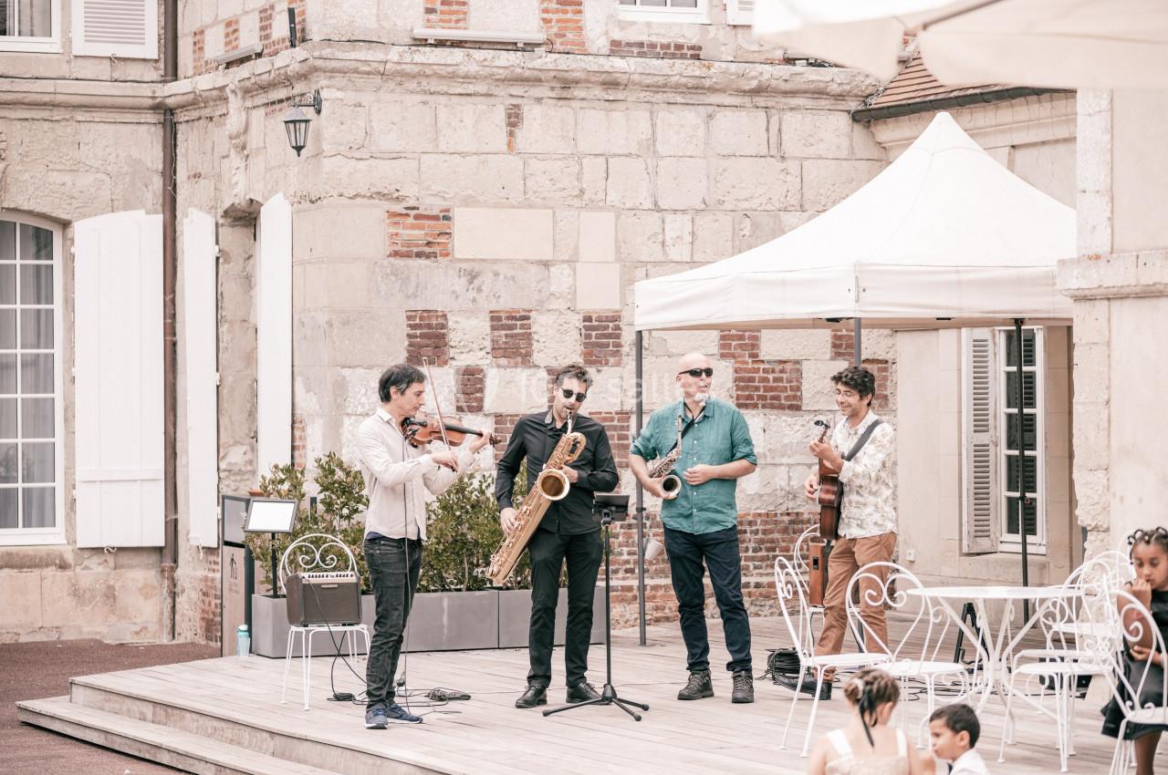 Un groupe de musiciens joue en plein air sur une petite scène devant un bâtiment en pierre.