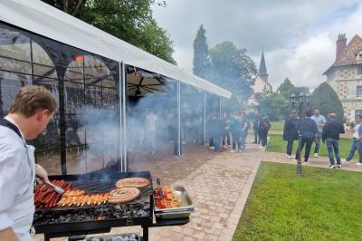 Des convives discutent près d'un barbecue en plein air, sous des parasols éclairés, dans une ambiance nocturne festive.