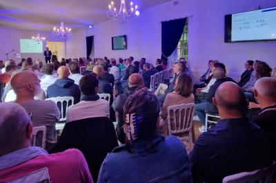 Des convives discutent près d'un barbecue en plein air, sous des parasols éclairés, dans une ambiance nocturne festive.