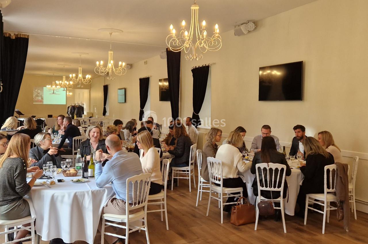 Des personnes assises autour de tables rondes dans une salle élégante avec chandeliers, rideaux noirs et écrans muraux.