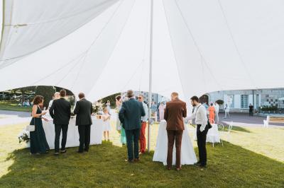 Des convives discutent près d'un barbecue en plein air, sous des parasols éclairés, dans une ambiance nocturne festive.