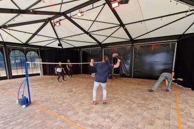 Des convives discutent près d'un barbecue en plein air, sous des parasols éclairés, dans une ambiance nocturne festive.