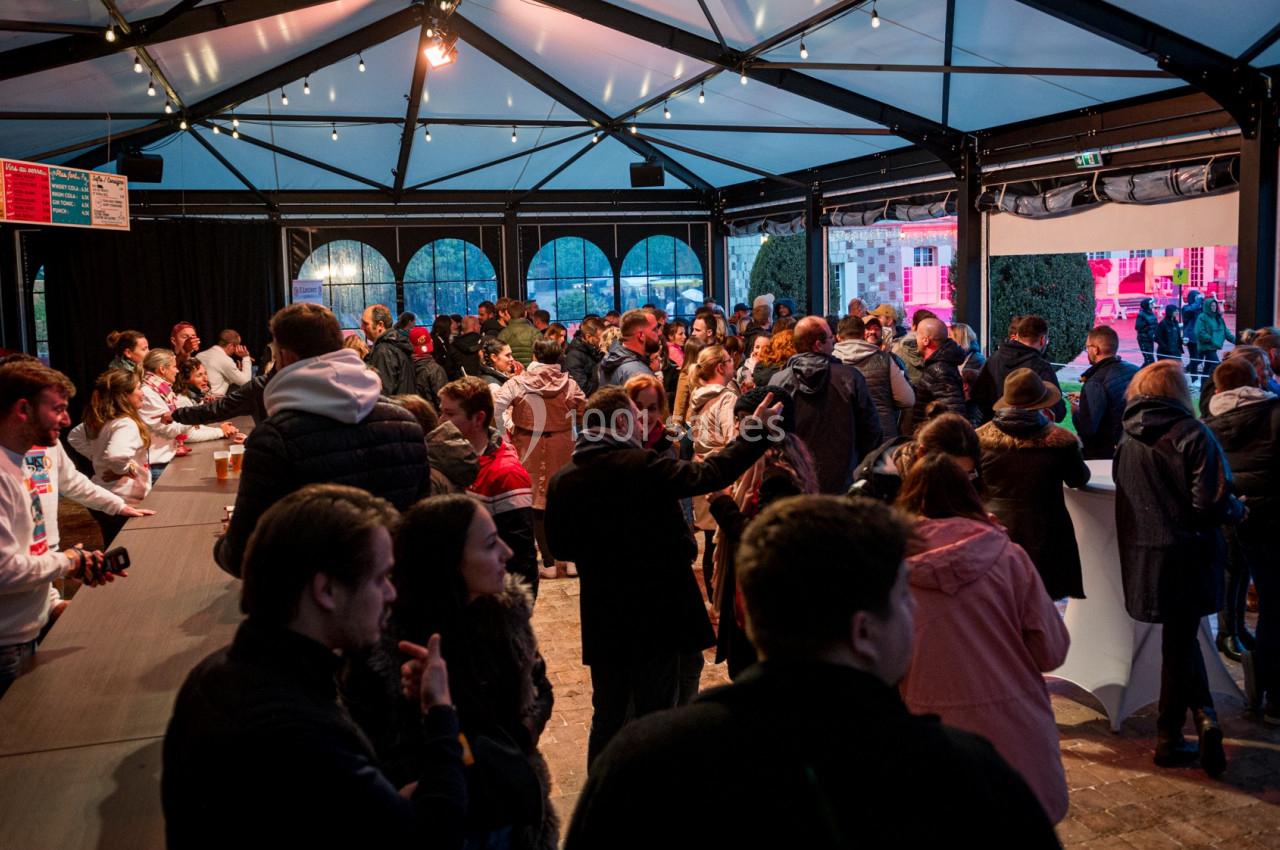 Groupe de personnes rassemblées sous une structure couverte, près d'un comptoir, dans une ambiance conviviale.