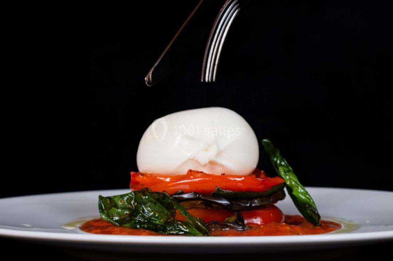 Assiette de légumes grillés superposés avec une boule de mozzarella, garnie de feuilles de basilic et sauce tomate.