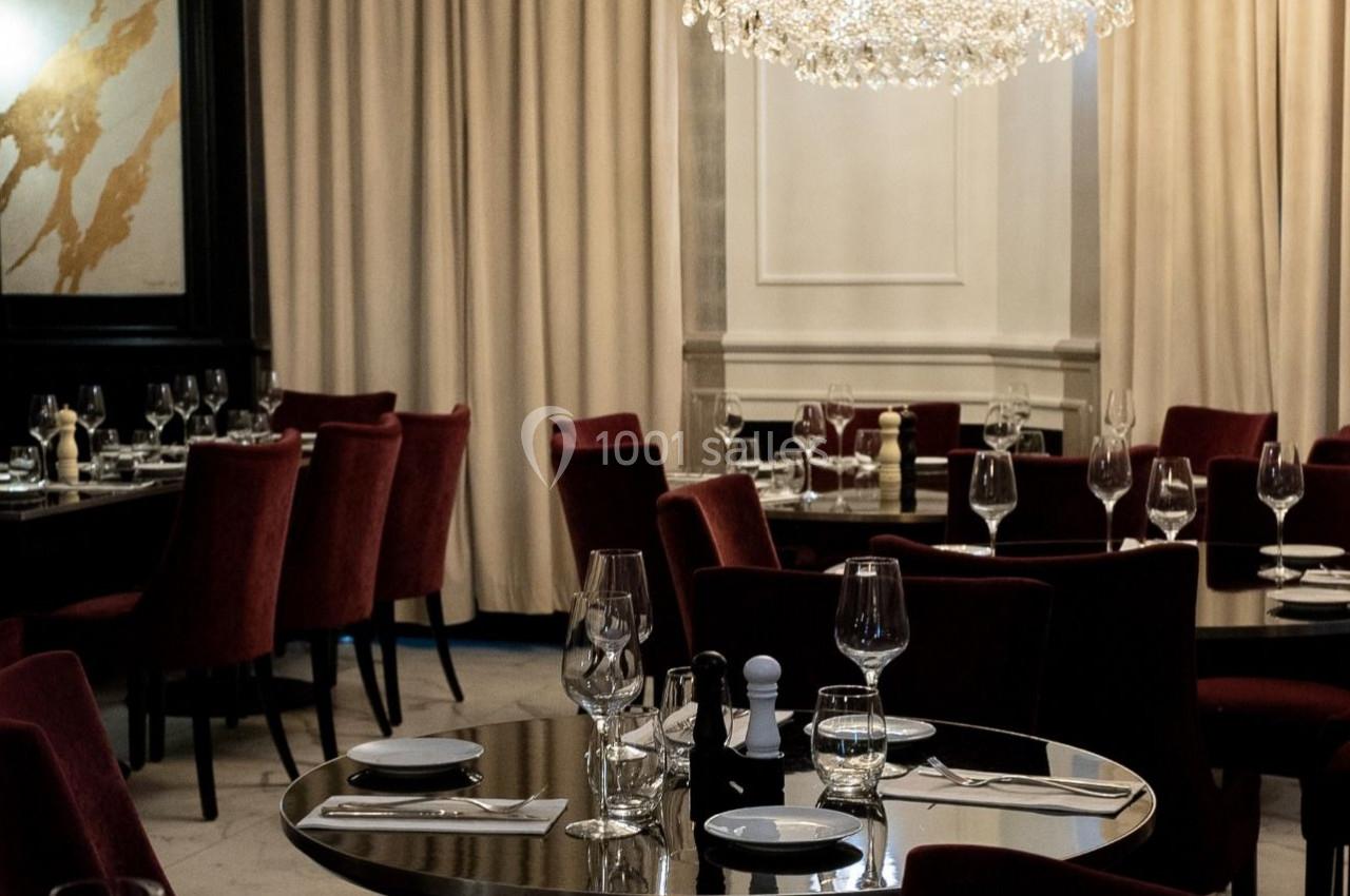 Salle de restaurant élégante avec tables dressées, chaises en velours rouge et lustre en cristal.