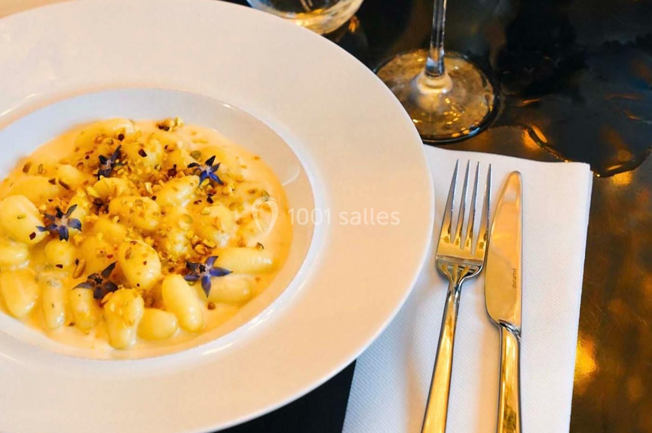 Assiette de gnocchis crémeux garnis de fleurs comestibles et éclats de noix, servie sur une table élégante.