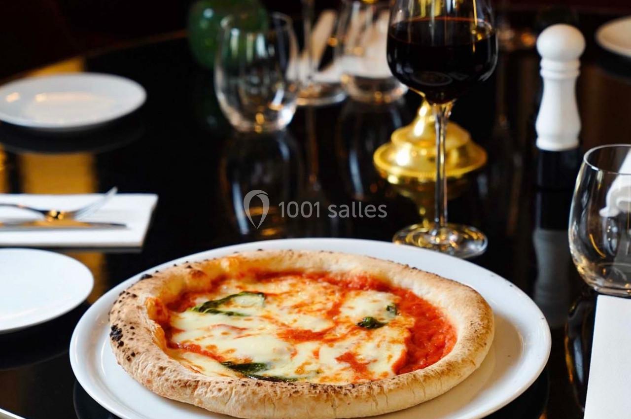 Pizza margherita servie sur une table élégante avec verre de vin rouge, couverts et assiettes en arrière-plan.