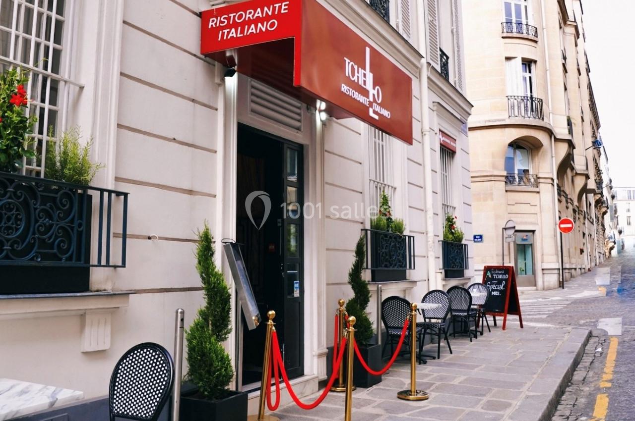 Façade d'un restaurant italien avec terrasse, enseigne rouge et plantes en pots, situé dans une rue pavée.
