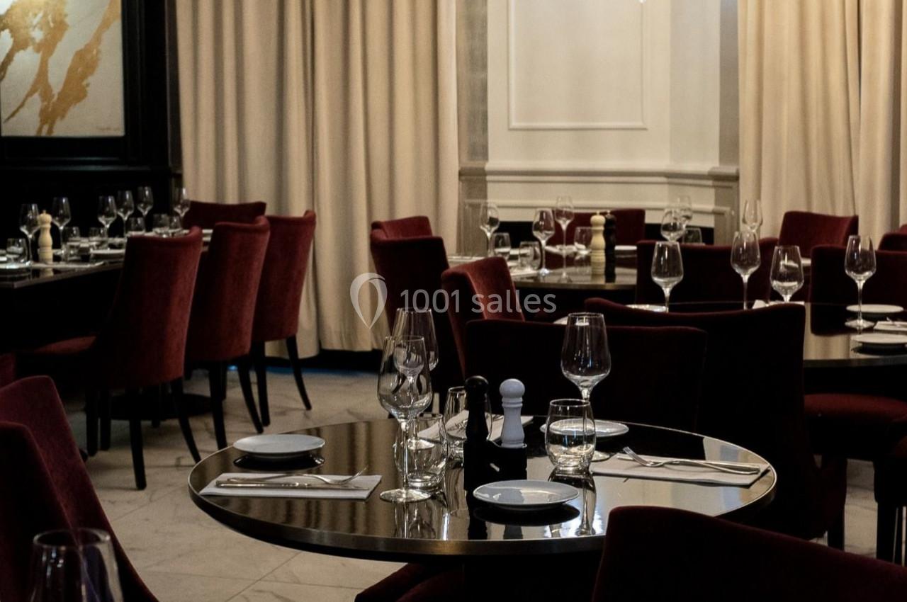 Salle de restaurant élégante avec tables dressées, nappes blanches, verres et chaises en velours rouge.